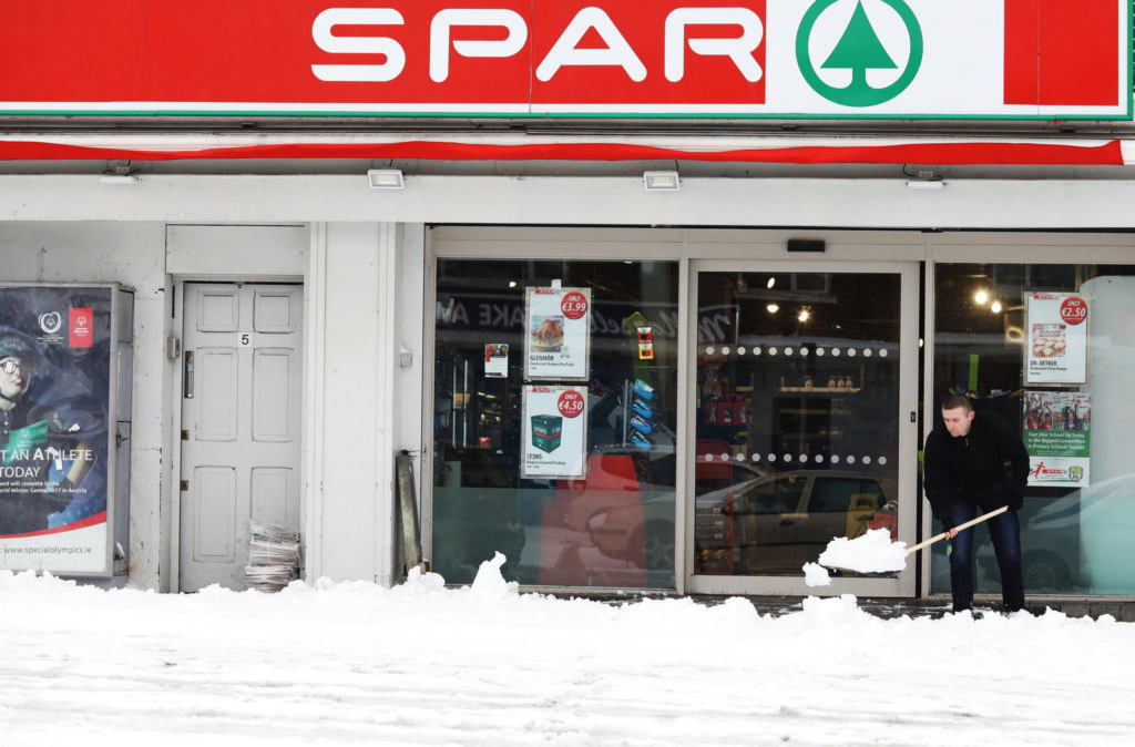 A man clears snow off the pathway outside Spar in Glasnevin, Dublin, after blizzard conditions the previous night